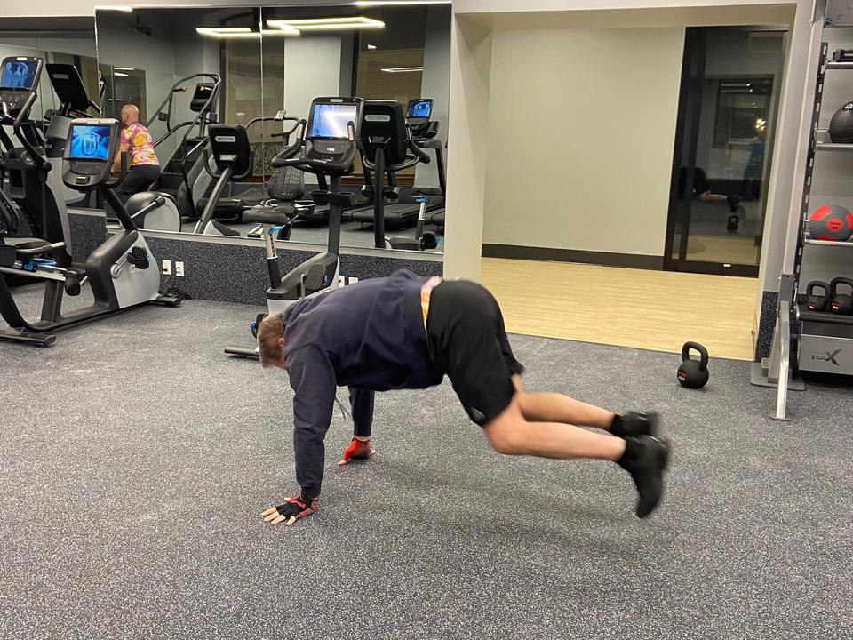 Man doing a plank-style exercise on the studio floor, with cardio machines behind him